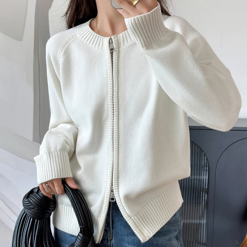allvariants:: Person wearing a white zip-up sweater holding a black handbag indoors.