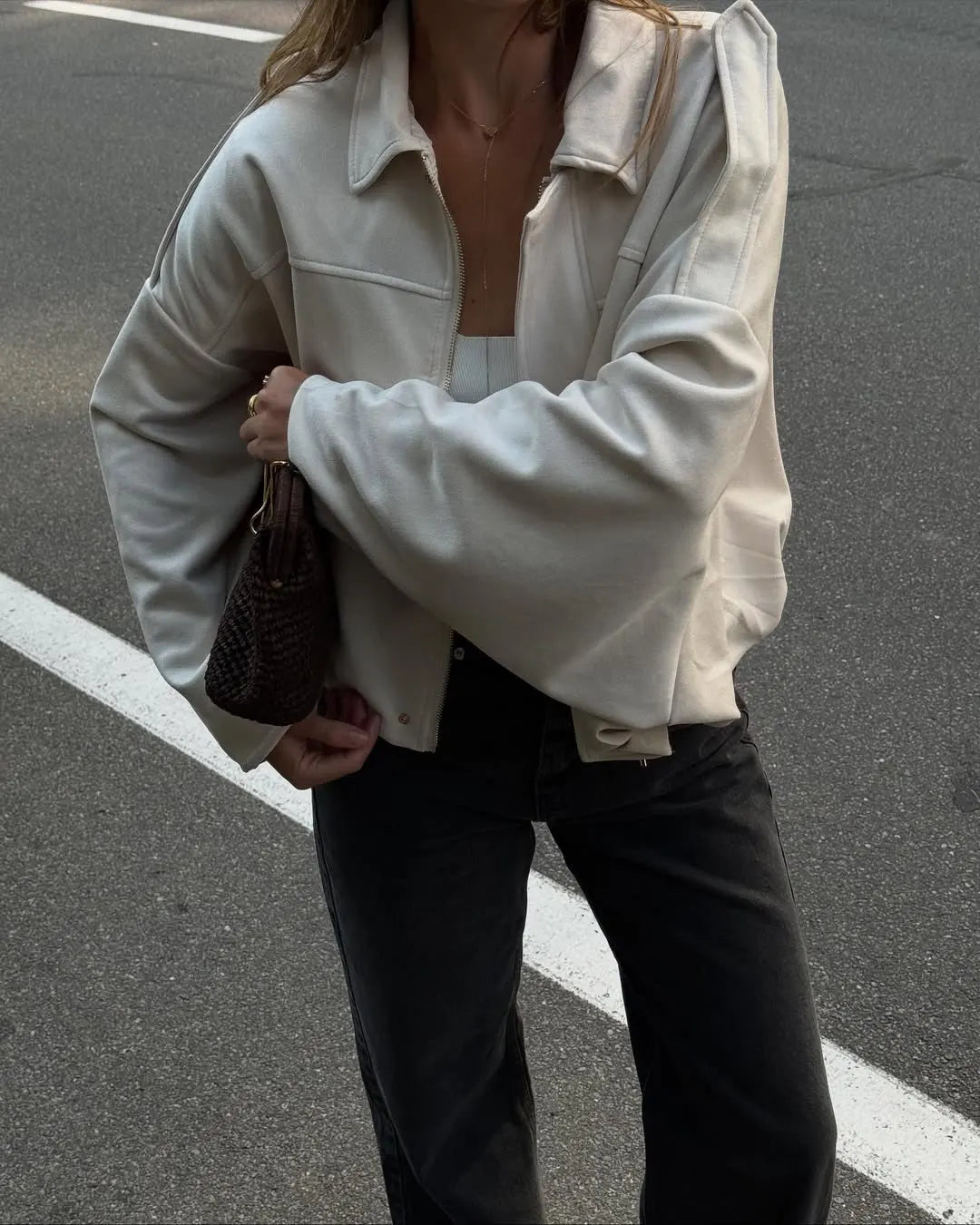 beige::Person wearing a light-colored jacket and dark pants on a street.