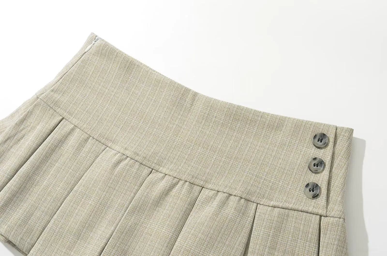 allvariant::Close-up of beige pleated shorts with buttons on a white background
