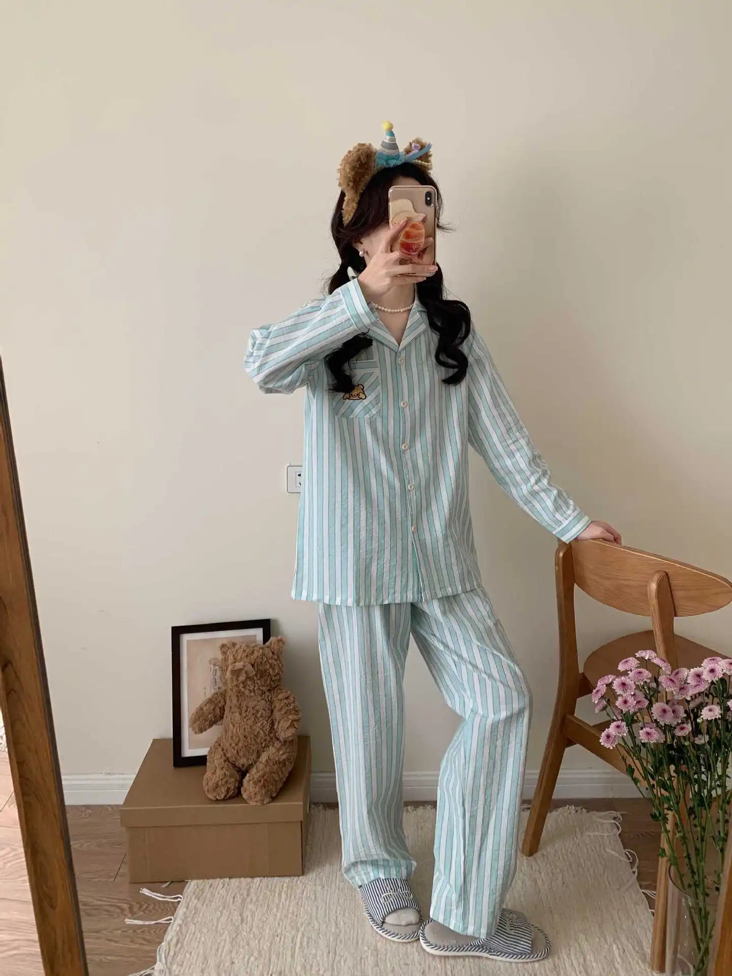 02:: Person wearing a striped pajama set in a room with a teddy bear and flowers.