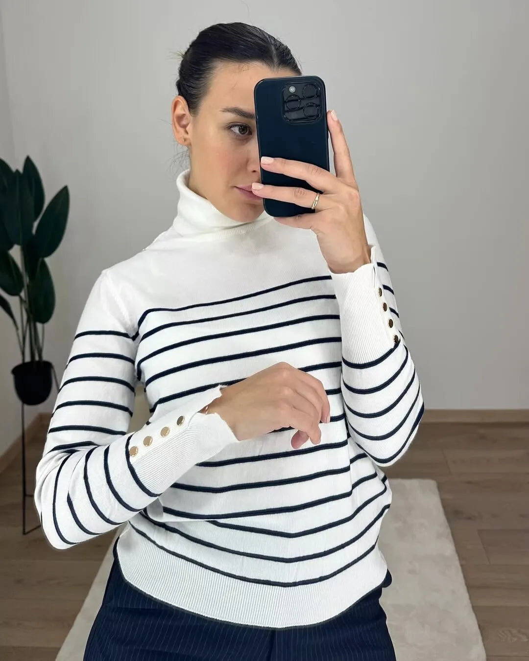 allvariant::Person wearing a white and black striped sweater with gold buttons, taking a mirror selfie.