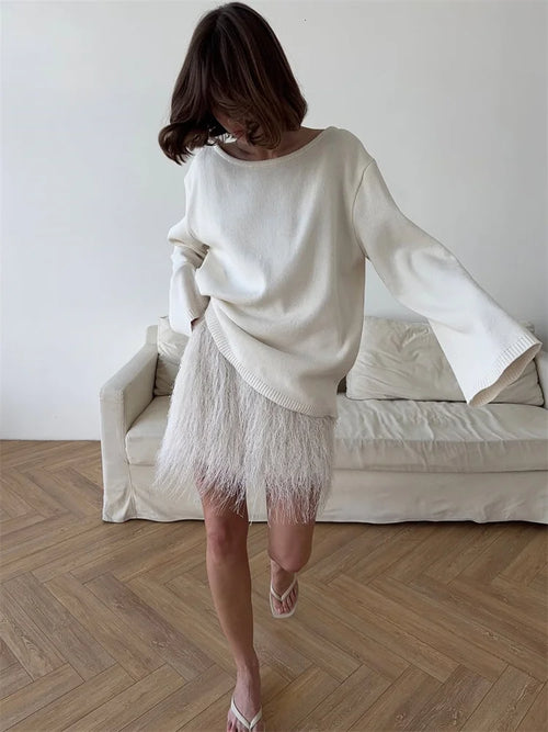 allvariants:: Woman wearing a white sweater and feathered skirt in a minimalistic room.