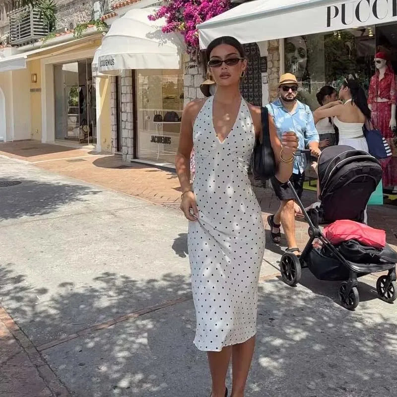 white::Woman in a white polka dot dress walking on a street with shops in the background