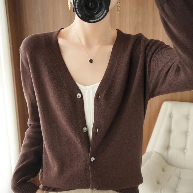allvariants:: Person wearing a brown cardigan over a white top, standing in a room with a wooden wall and white furniture.