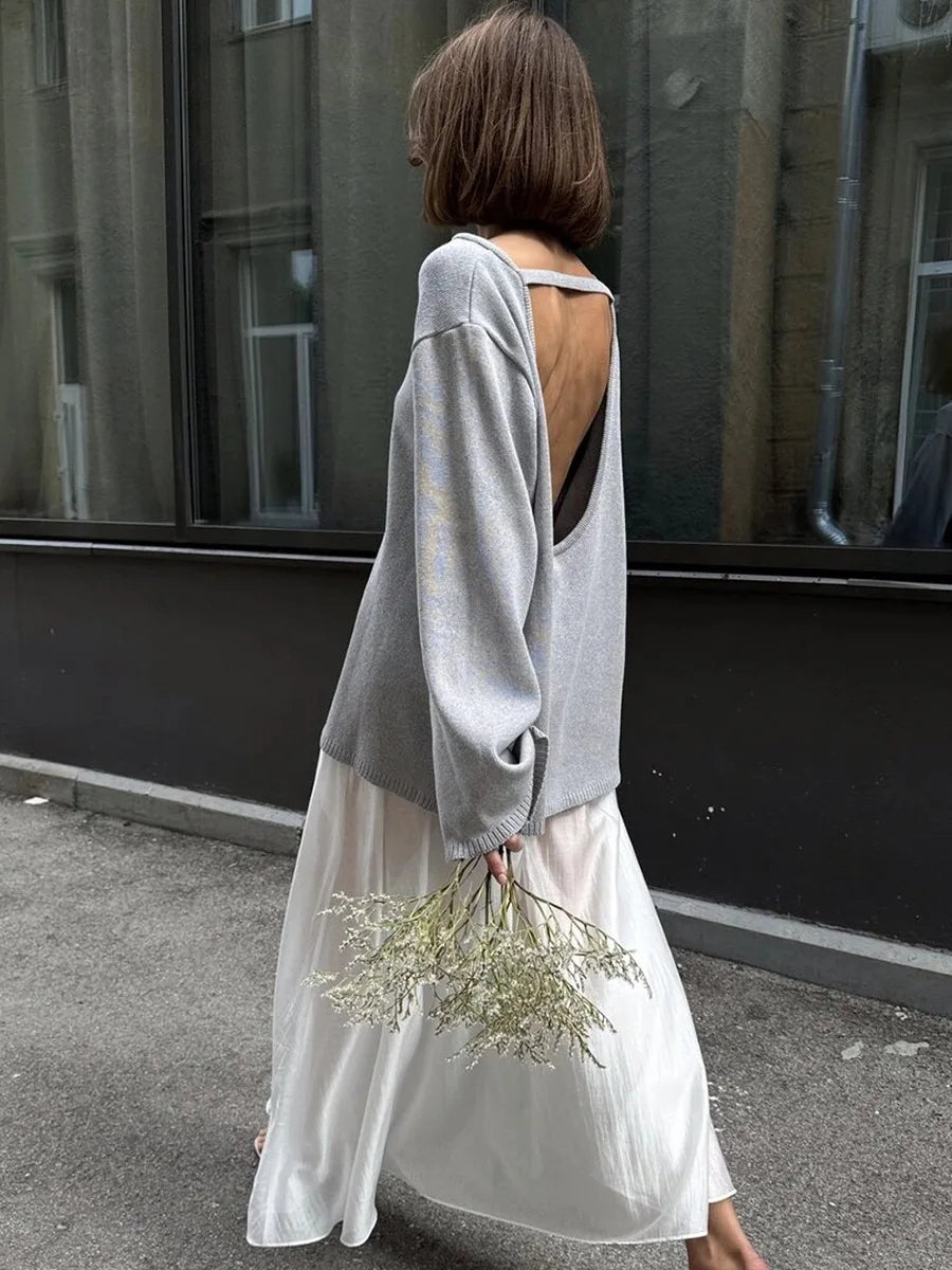 allvariants:: Woman wearing a light gray sweater with cut-out design and a white skirt, holding dried flowers, standing on a street.