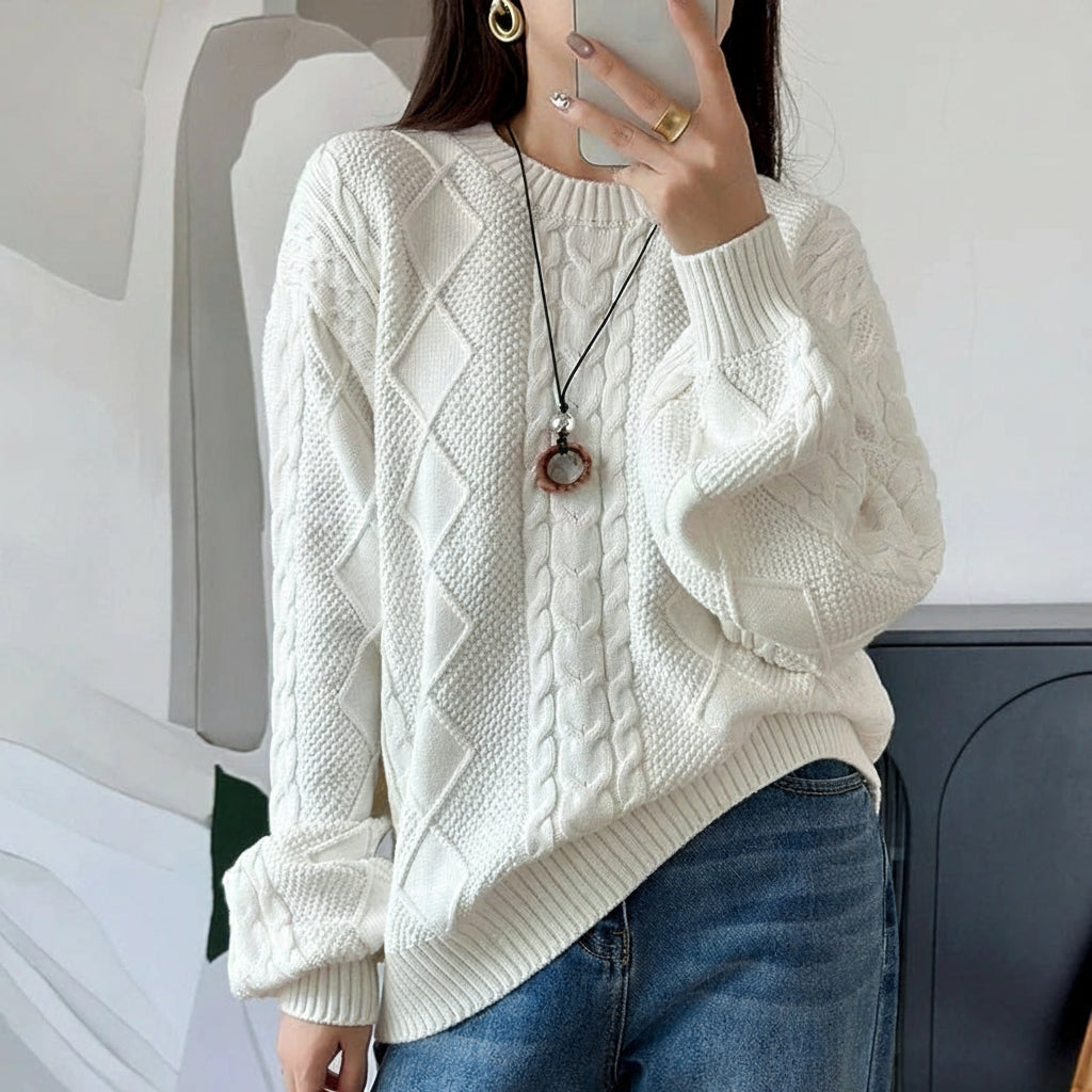 White:: Person wearing a white cable knit sweater and blue jeans, holding a phone.