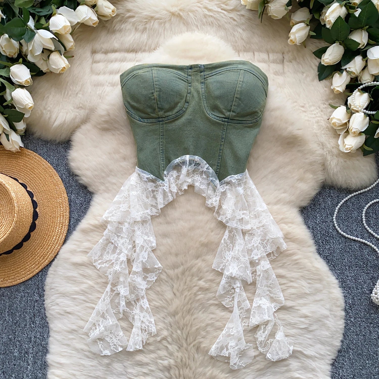 allvariants:: Green strapless top with lace details on a fluffy white surface surrounded by white flowers and a straw hat.