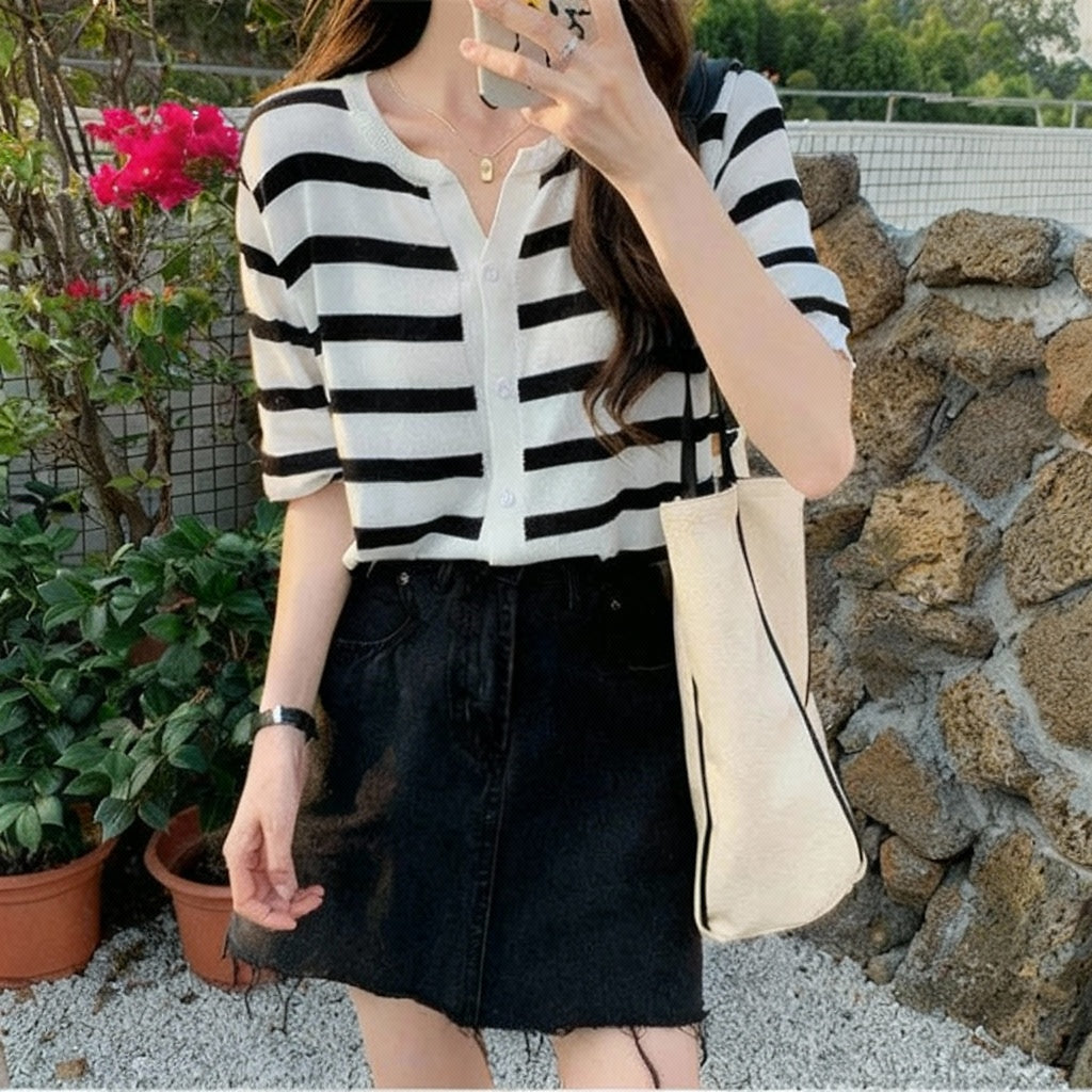 allvariants:: Woman taking a selfie outdoors with a striped cardigan and black skirt.
