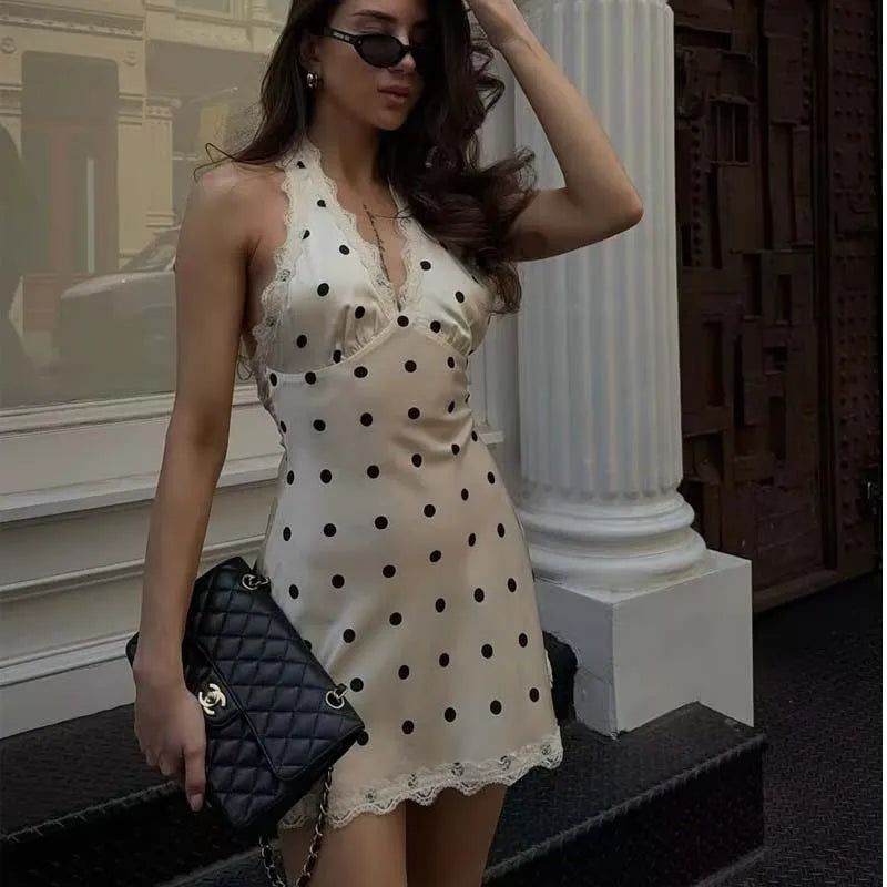 White::Woman in a polka dot dress holding a black handbag on a city street.