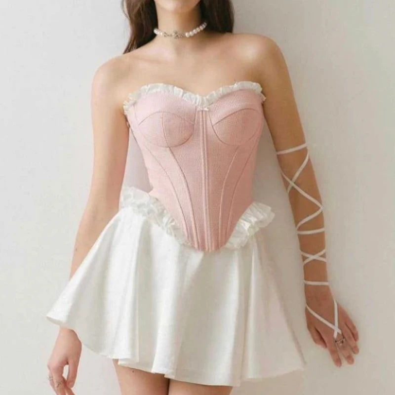 pink::Woman wearing a pink corset and white dress with sheer gloves against a plain background