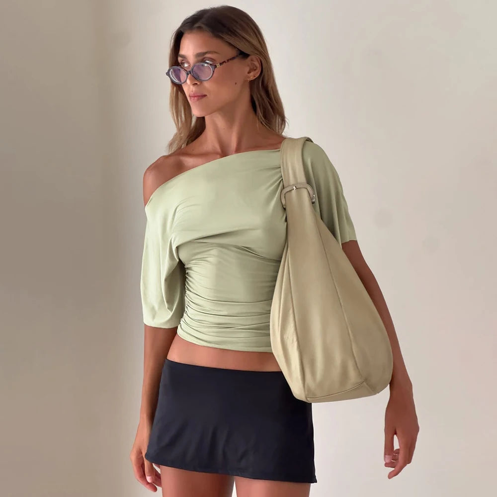green::Woman wearing a light green top and black skirt, carrying a beige bag against a plain background