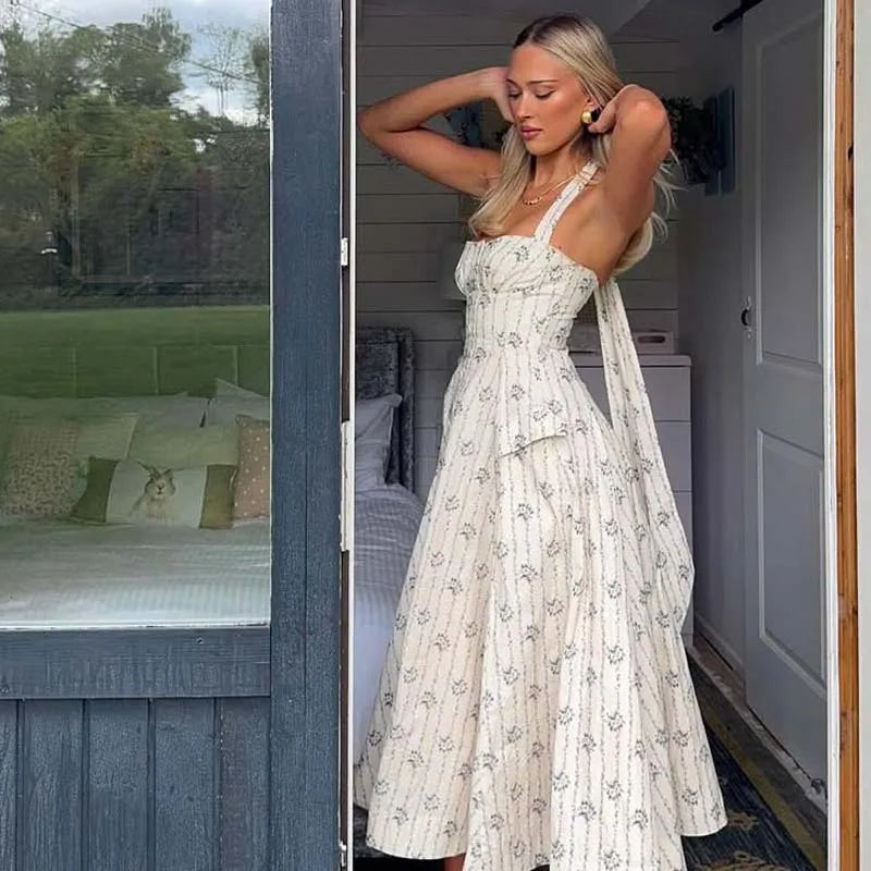 flora::Woman in a floral dress standing in a doorway with a garden view outside.