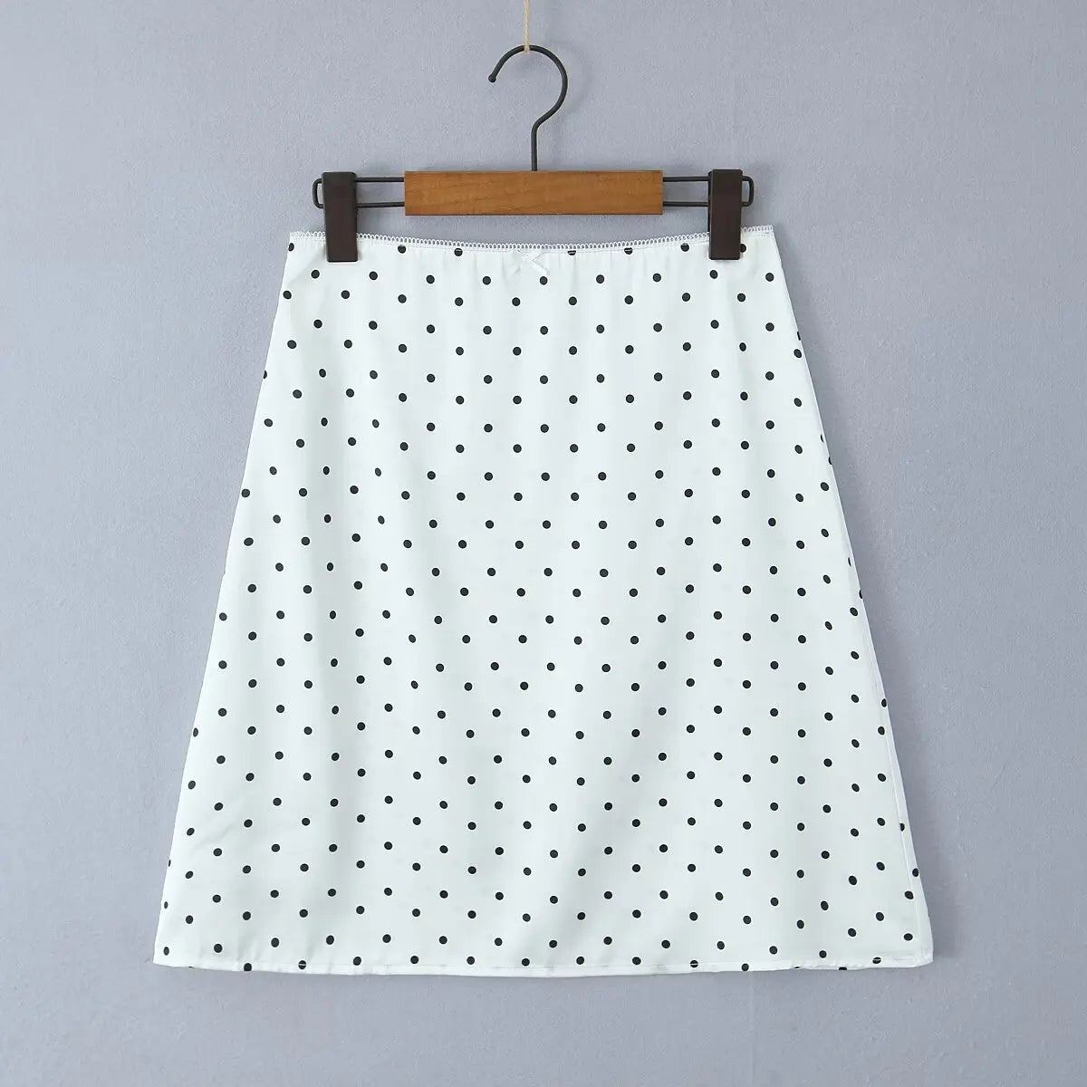 white::White skirt with black polka dots on a hanger against a gray background