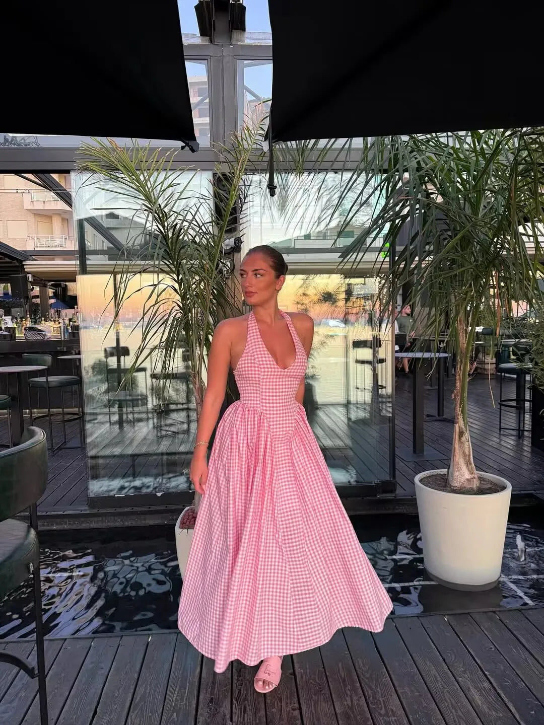 pink::Woman in a pink dress standing on a wooden deck with plants and tables in the background