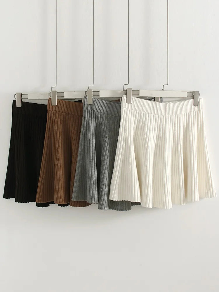 allvariants:: Four pleated skirts in black, brown, gray, and white hanging on a rack against a white background.