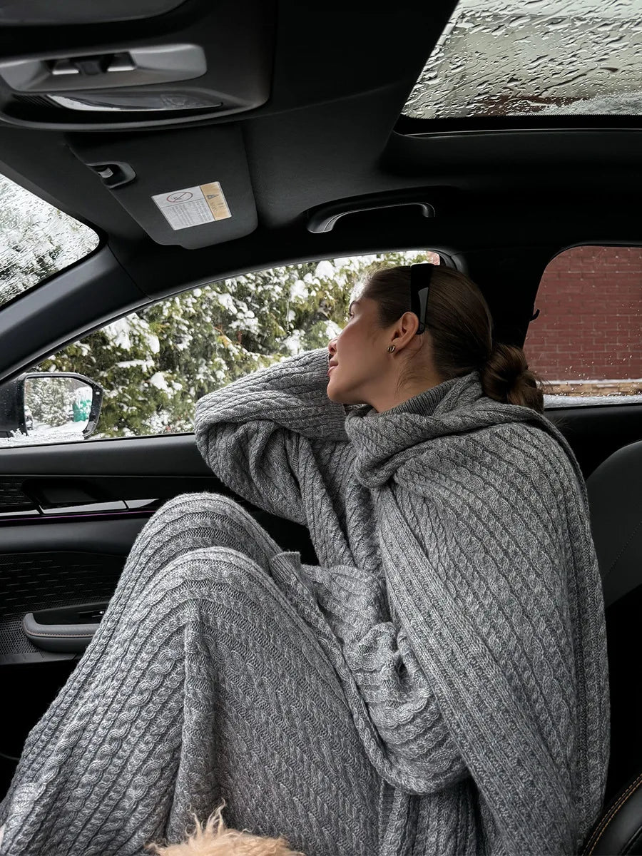 Gray:: Person sitting in a car wearing a gray knit sweater and pants, with snow outside.