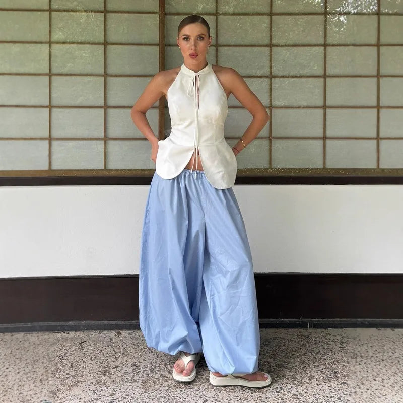 sky blue::Person wearing a white sleeveless top and light blue wide-leg pants standing against a tiled wall.