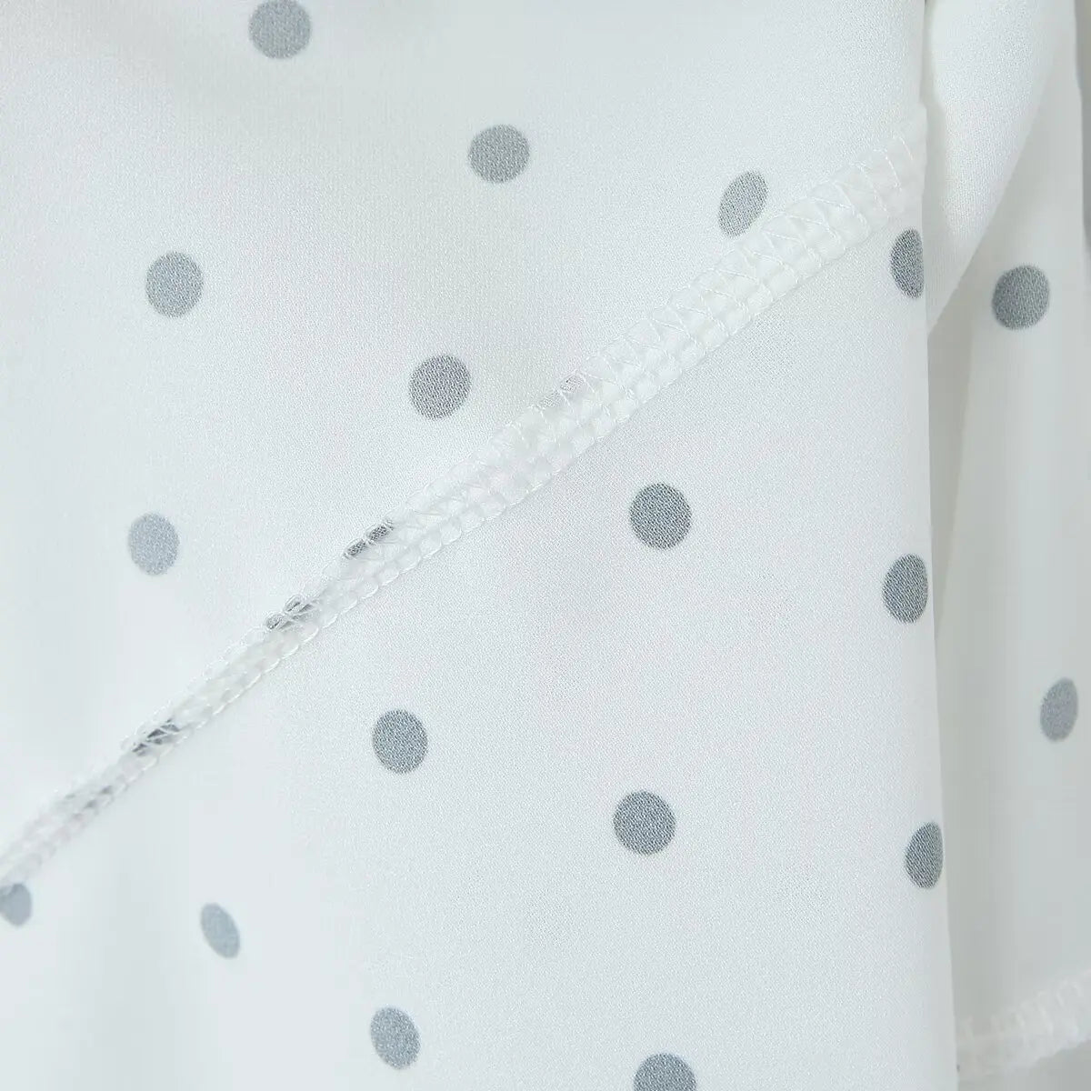 white::Close-up of a white fabric with gray polka dots and visible stitching.