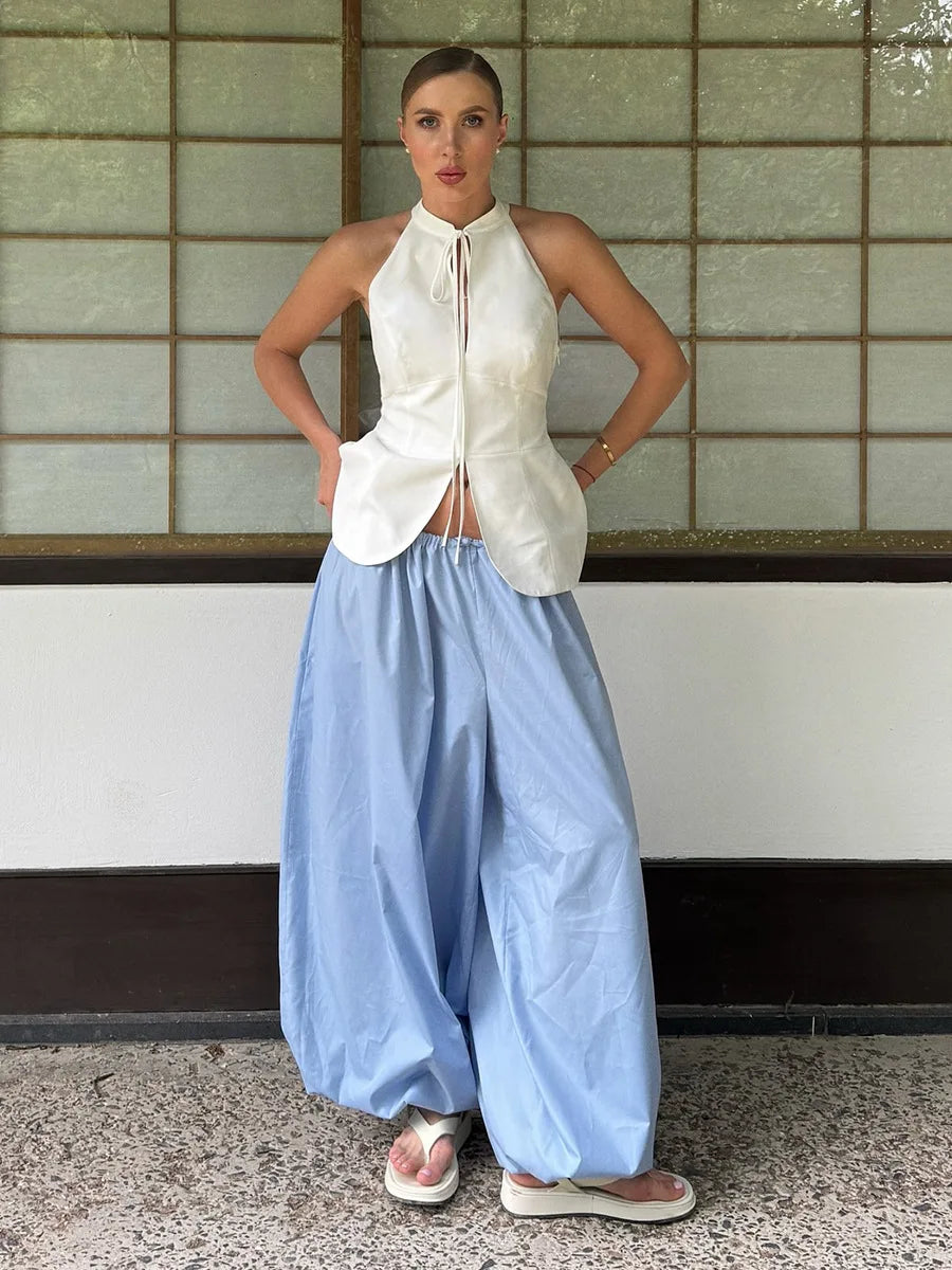 light blue::Person wearing a white sleeveless top and light blue wide-leg pants standing against a tiled wall.