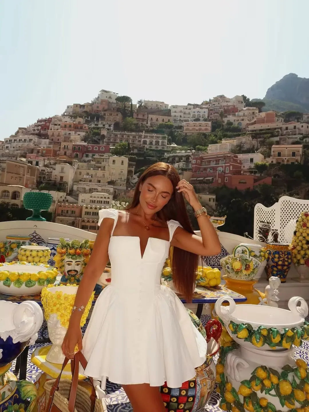 white::Woman in a white dress standing in front of a scenic view with buildings and mountains.
