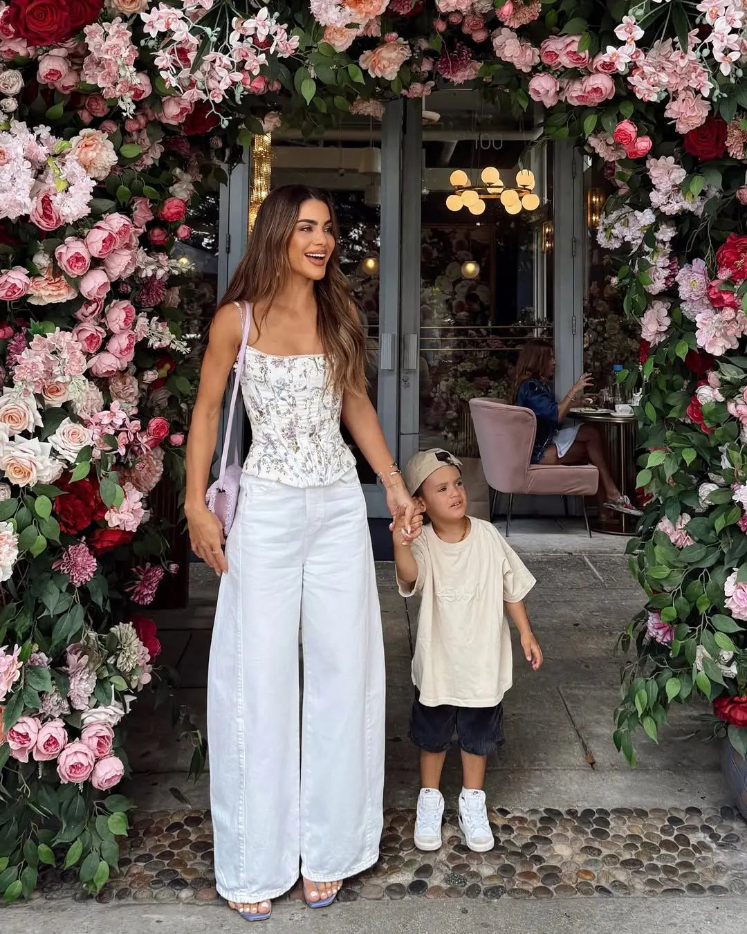 white::Woman and child holding hands in front of a floral archway