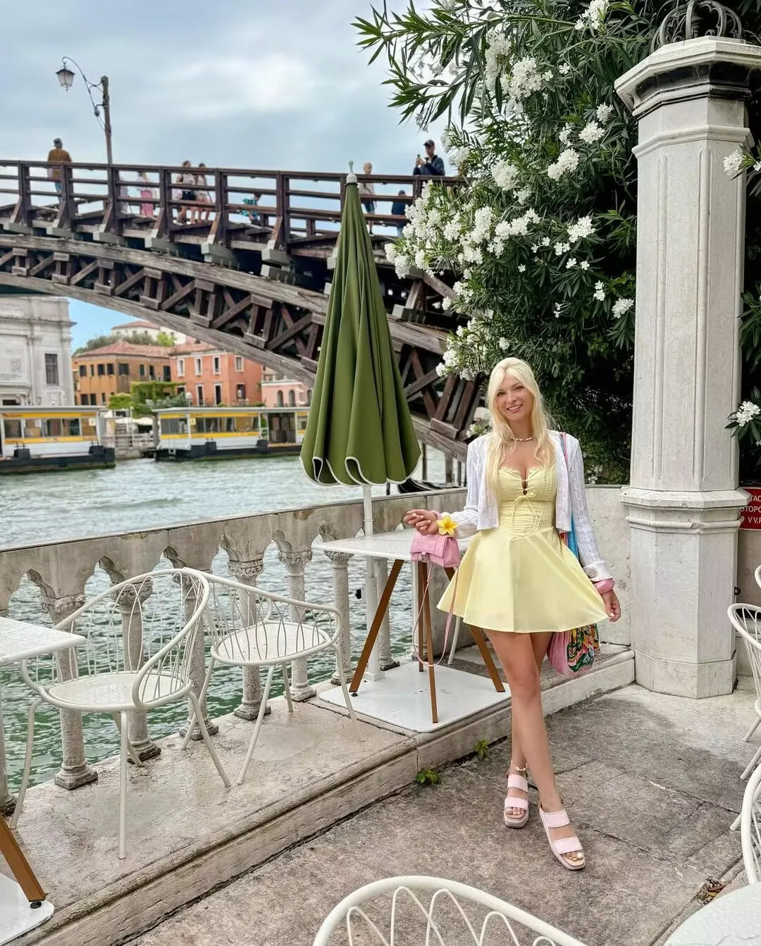 yellow::Woman in a yellow dress standing by a waterfront with a bridge and canal in the background