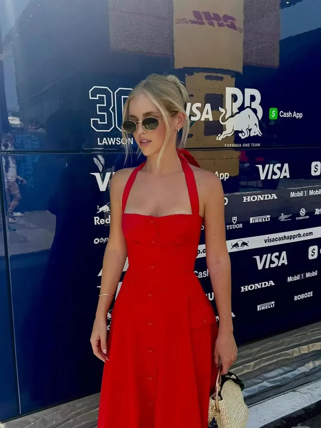 red::Woman in a red dress standing in front of a Formula 1 team truck with various sponsor logos.