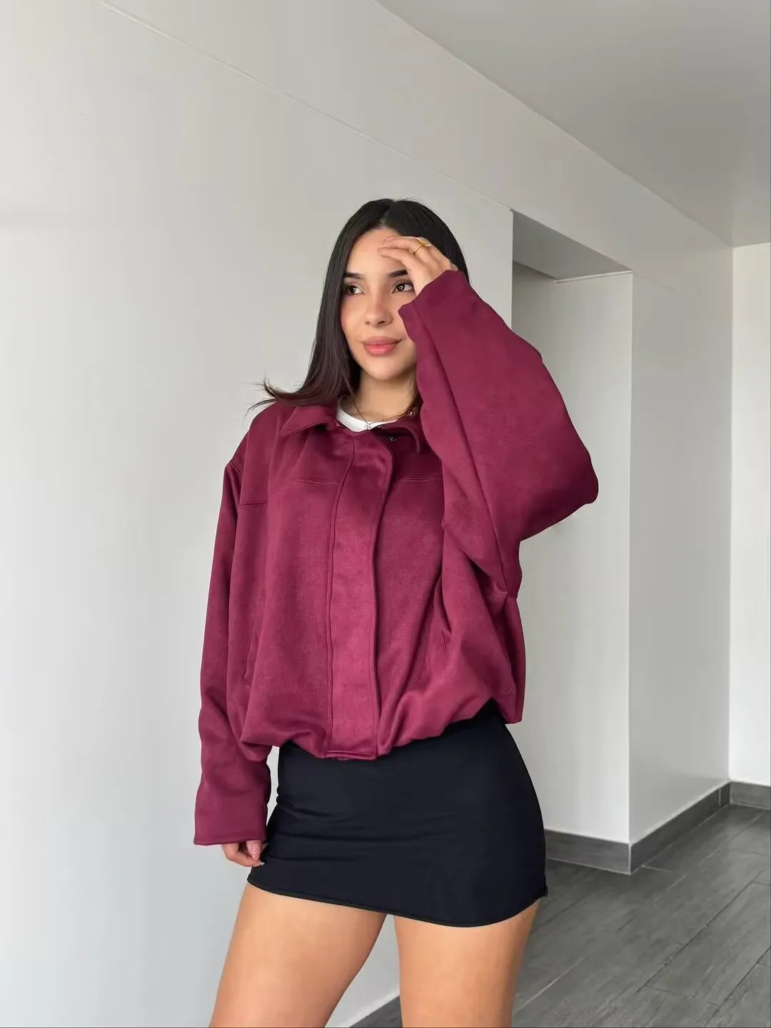 burgundy::Person wearing a maroon jacket and black skirt indoors.