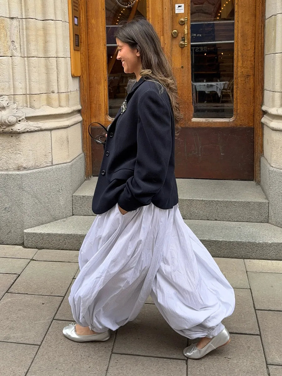 light blue::Woman in a black jacket and white pants walking on a sidewalk.