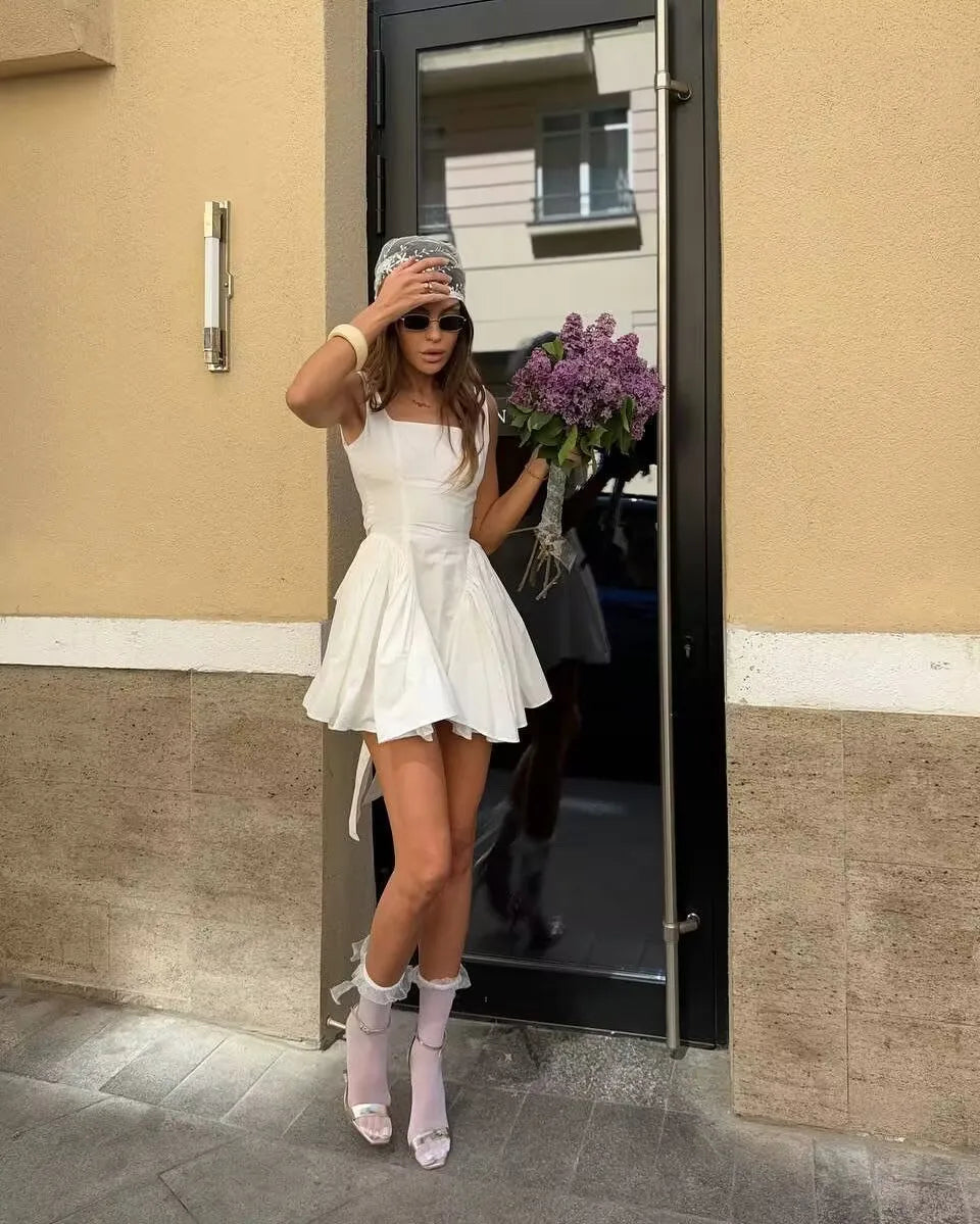 white::Woman in a white dress standing outside a building holding flowers.