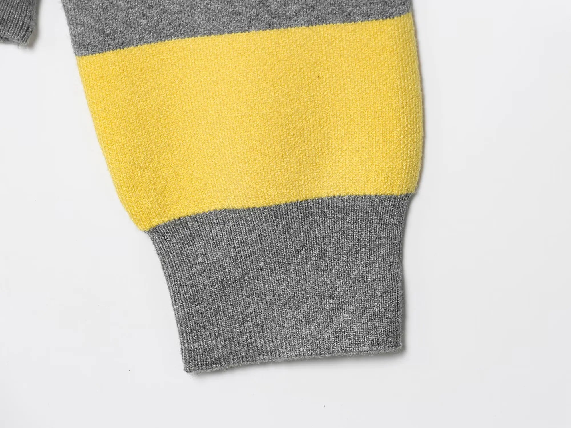 stripped::Close-up of a sweater with gray and yellow color block design on a light gray background