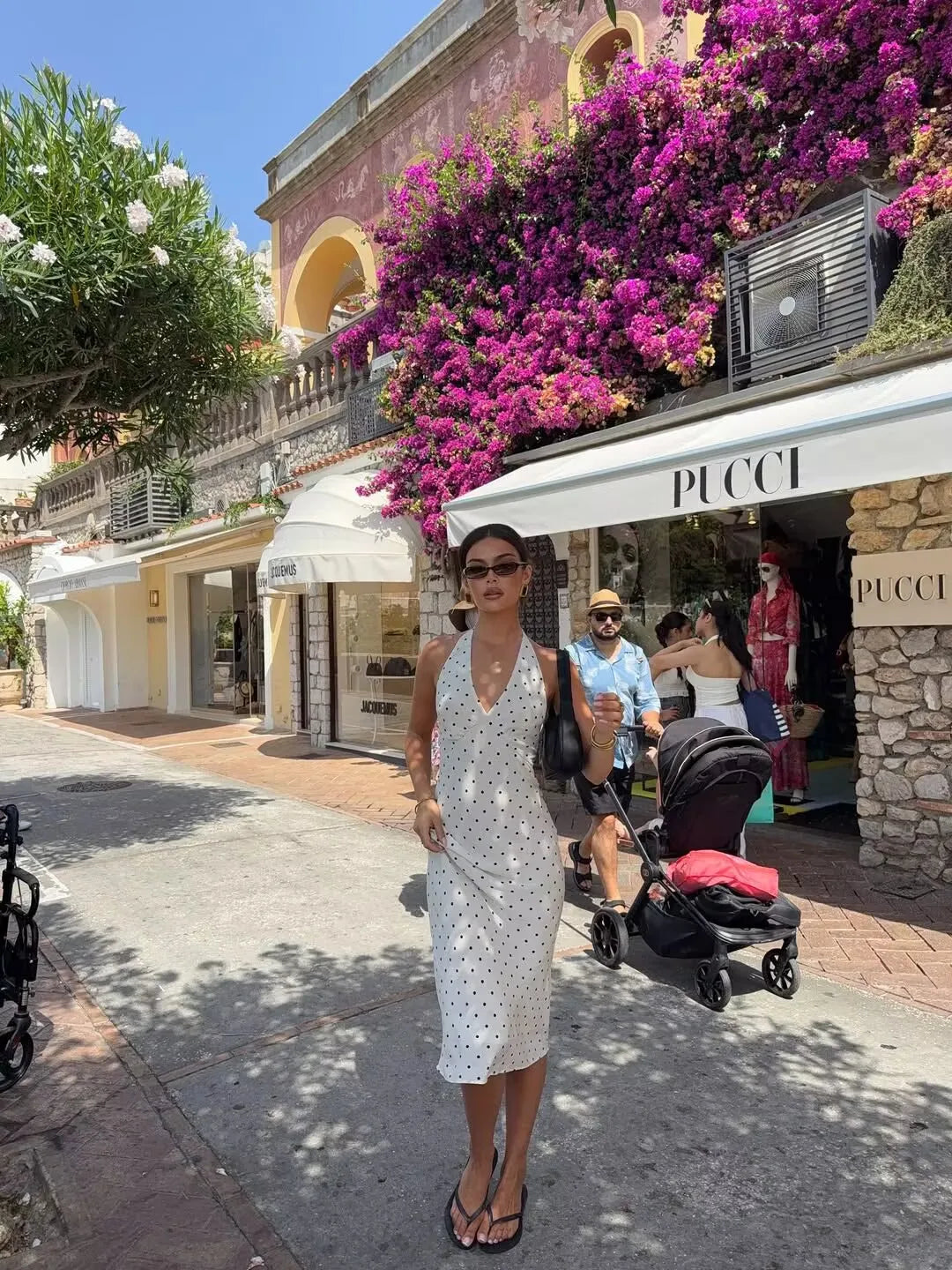 white::Woman in a white dress standing in front of a Pucci store with purple flowers above.