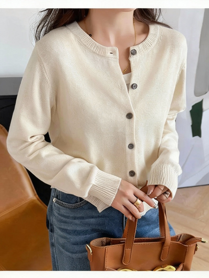 Cream:: Person wearing a beige cardigan with black buttons, holding a brown handbag indoors.
