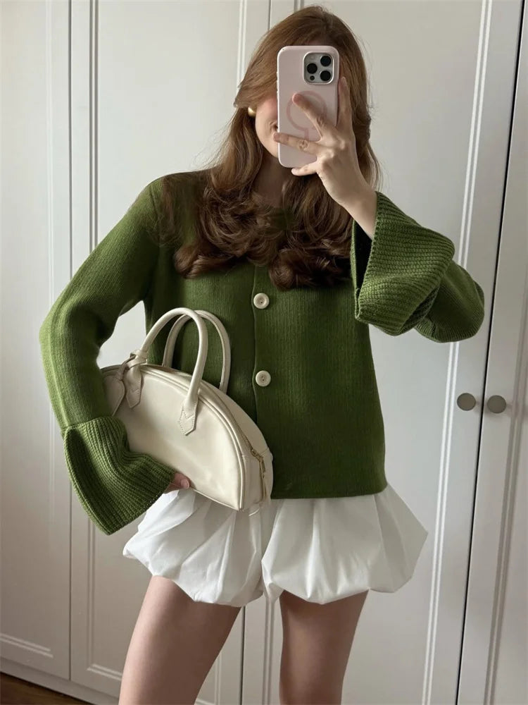 allvariants:: Person wearing a green sweater and white skirt holding a beige handbag.
