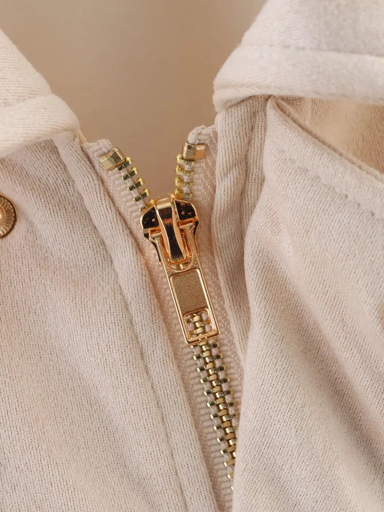 allvariant::Close-up of a gold zipper on a beige garment with a blurred background