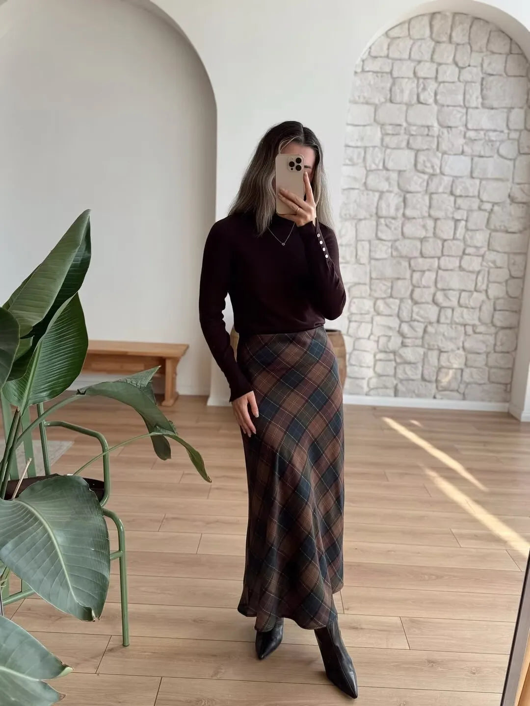 allvariant::Person wearing a dark sweater and plaid skirt in a room with a stone wall and wooden floor.