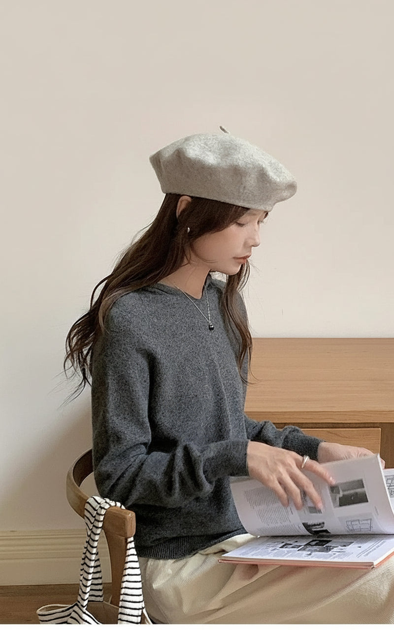 Dark Grey:: Woman wearing a gray sweater and beret reading a book in a room with wooden furniture.
