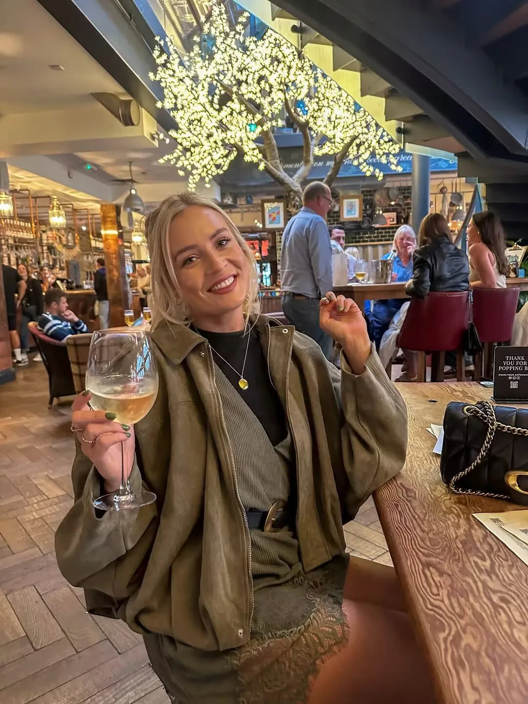 army green::Woman holding a glass of wine in a lively bar setting