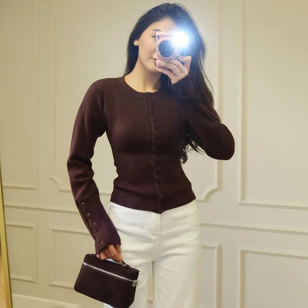 brown::Woman taking a mirror selfie wearing a brown sweater and white pants, holding a black handbag.