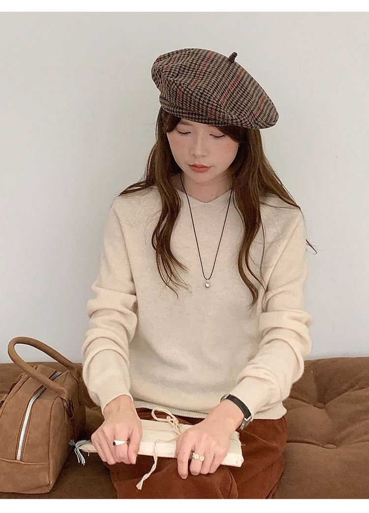 Beige:: Woman wearing a beige sweater and plaid beret sitting on a brown couch.