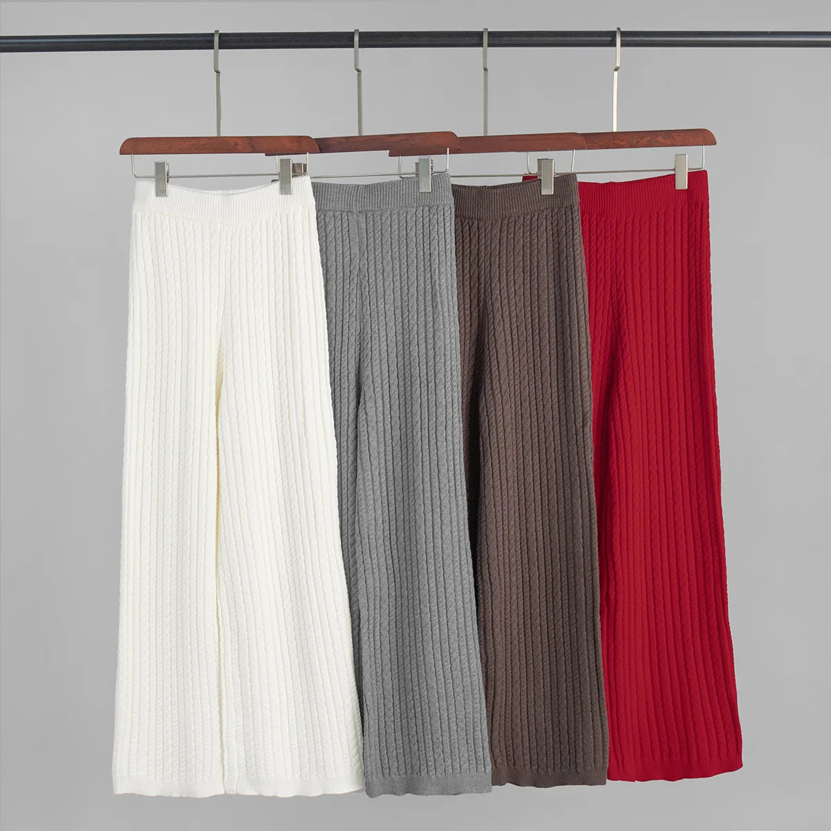 allvariants:: Four ribbed knit pants in white, gray, brown, and red hanging on a rack against a gray background.