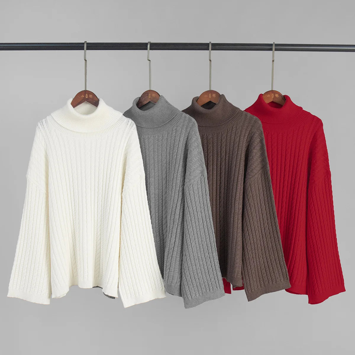 allvariants:: Four turtleneck sweaters in white, gray, brown, and red on hangers against a gray background.
