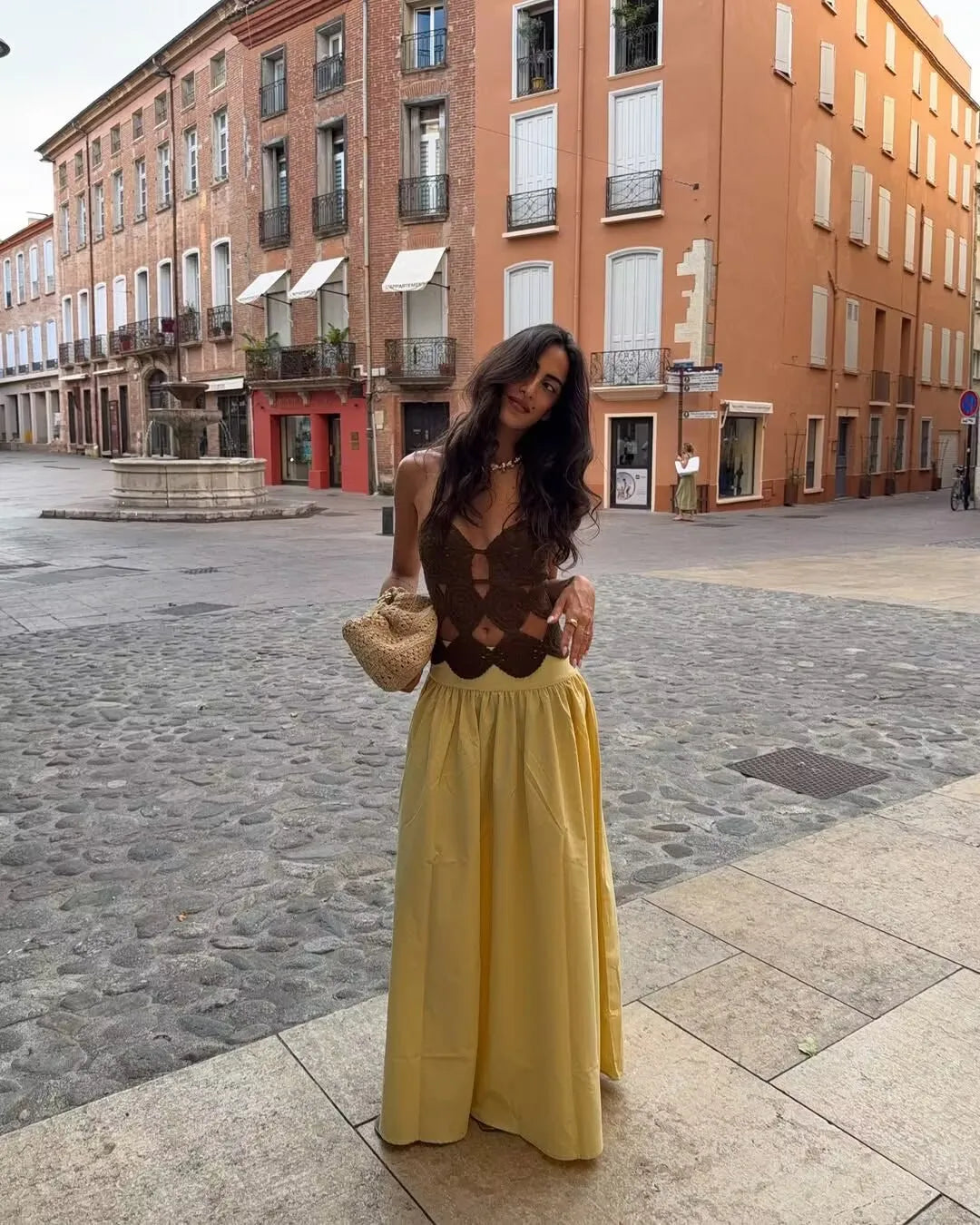 allvariant::Woman in a yellow dress standing on a street with buildings in the background