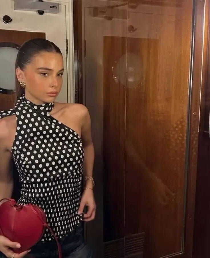 black::Woman in a polka dot top holding a red heart-shaped object in a room.