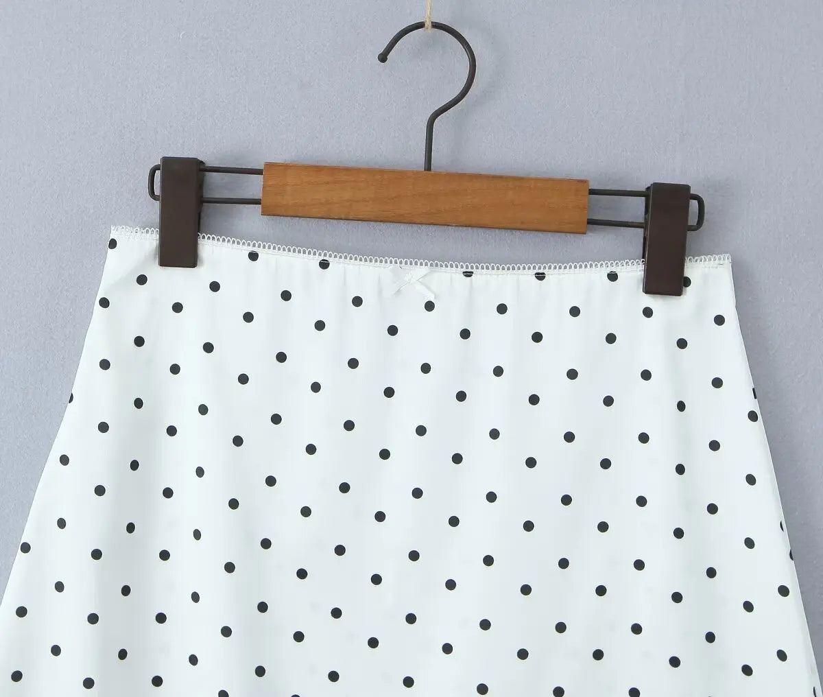 white::White skirt with black polka dots on a hanger against a gray background