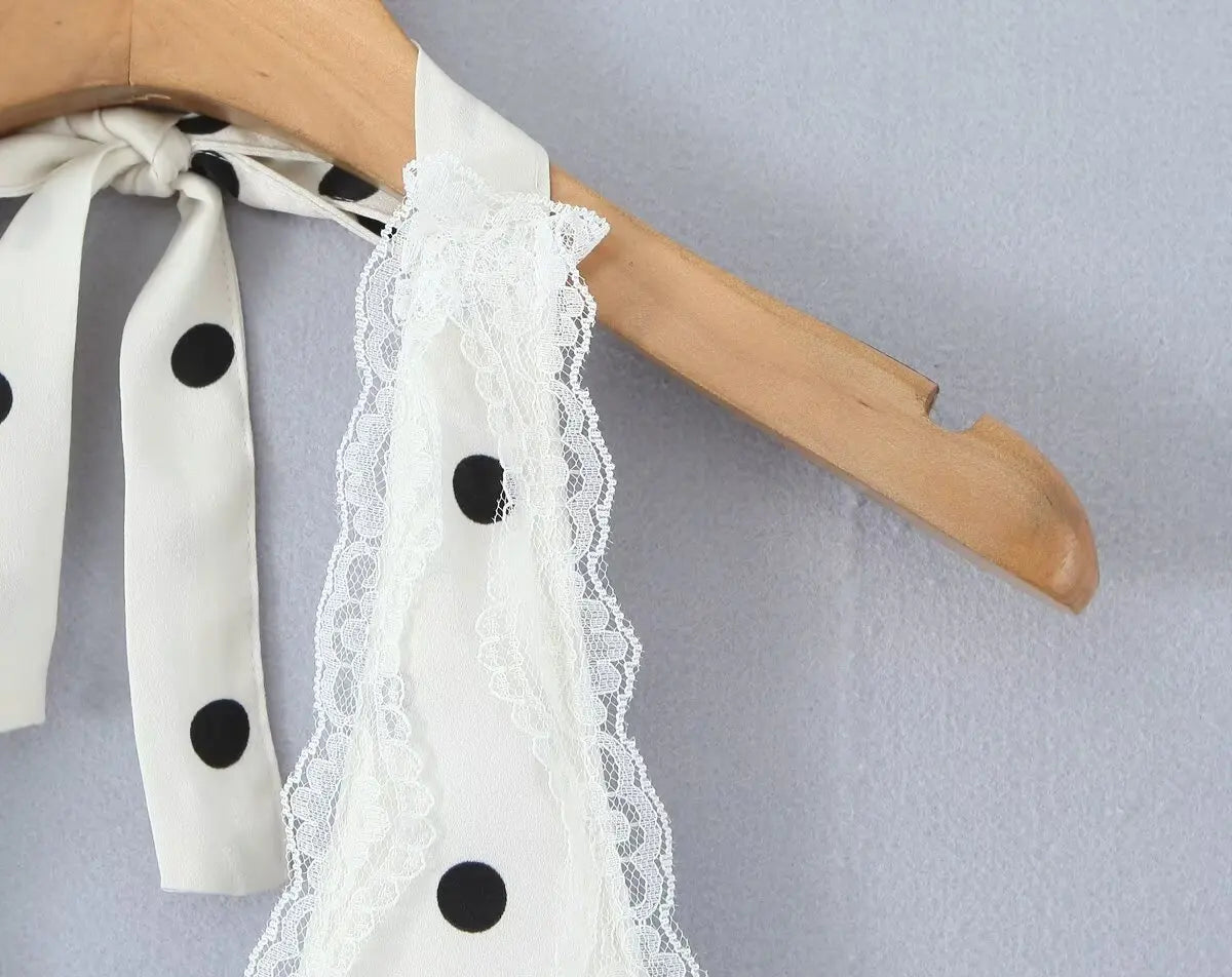 white::White blouse with black polka dots and lace details on a wooden hanger against a gray background