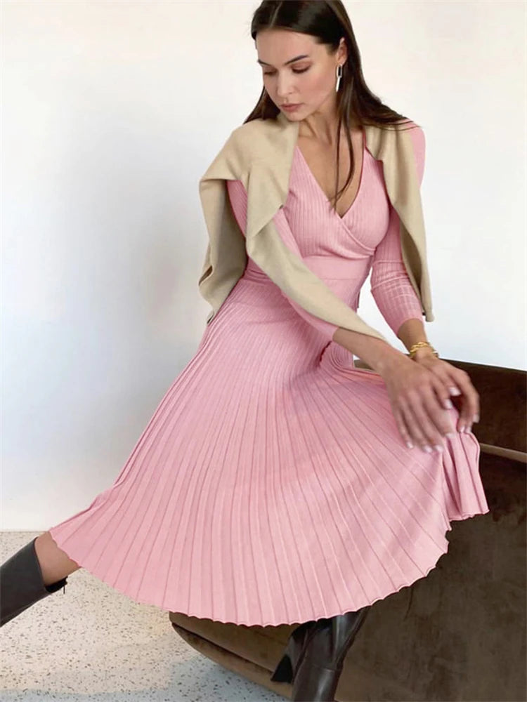 allvariants:: Woman wearing a pink pleated dress with a beige cardigan against a white background