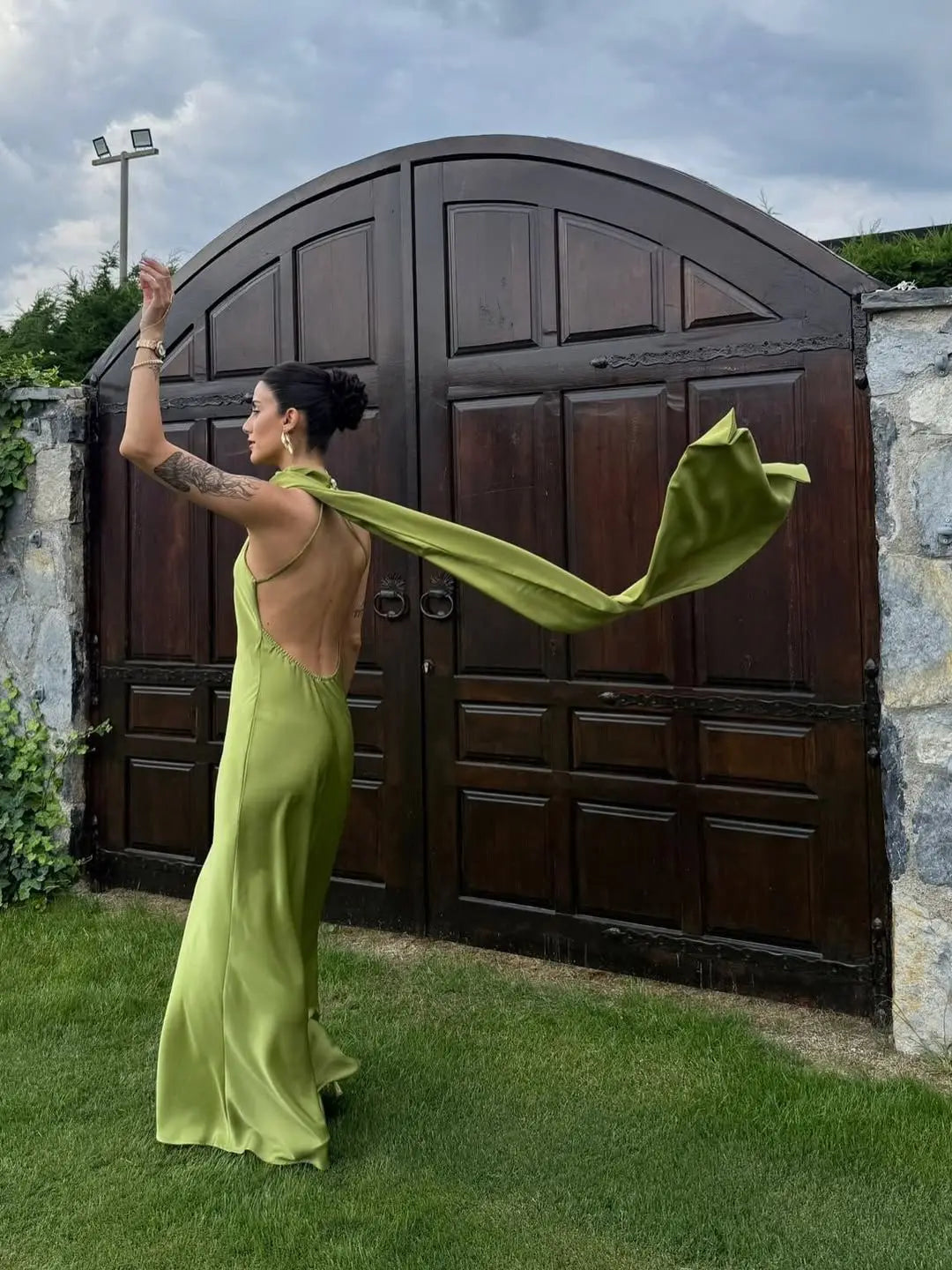 Green::Woman in a green dress with a long train standing in front of a large wooden gate.