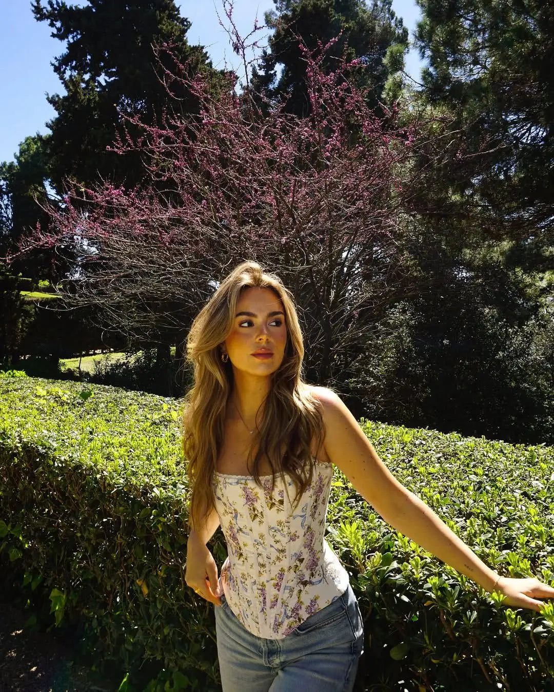white::Woman standing in a park with greenery and trees in the background