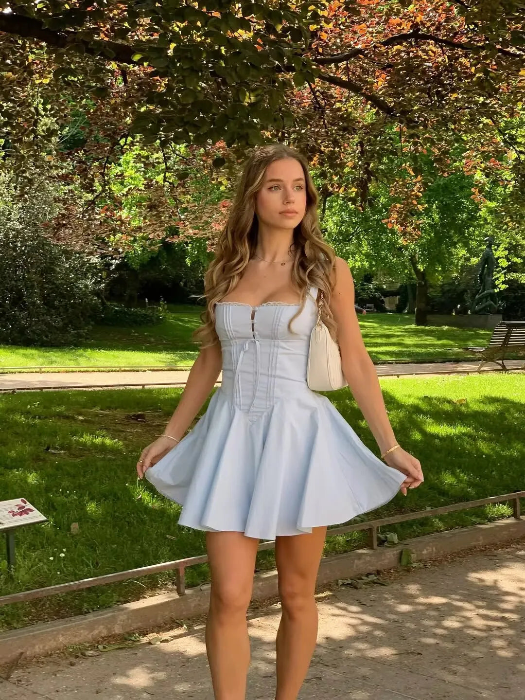 blue:: Woman in a light blue dress standing in a park with green grass and trees.